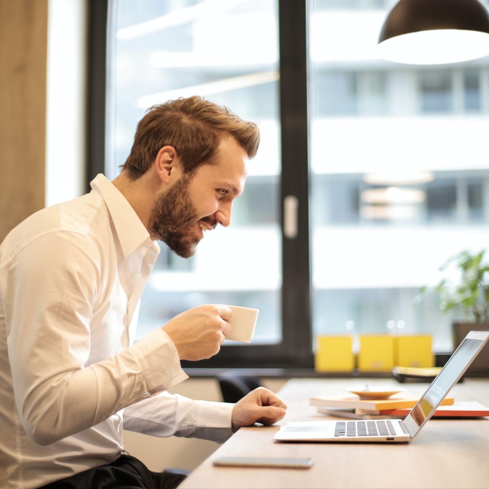 hombre tomando cafe frente a una laptop sonriendo